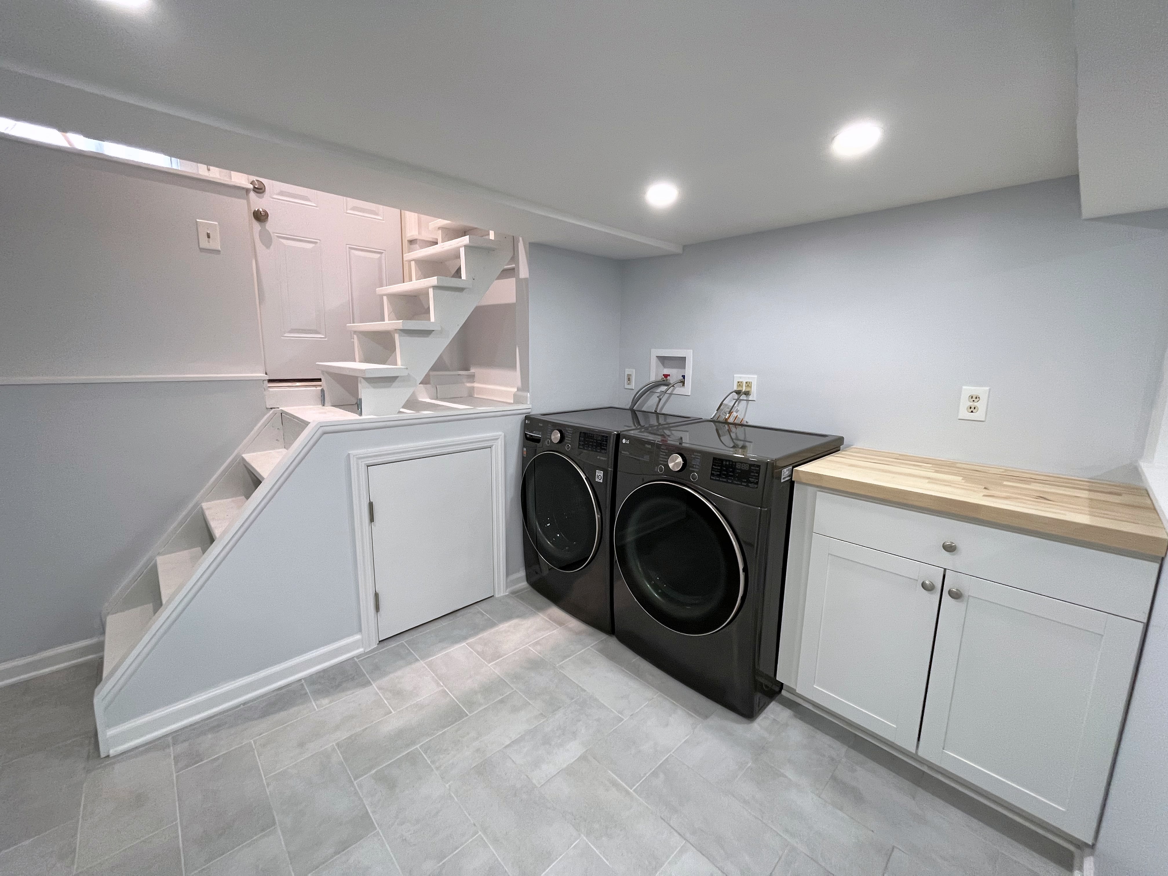 Finished basement laundry area with black washer, dryer, white cabinets, stairs